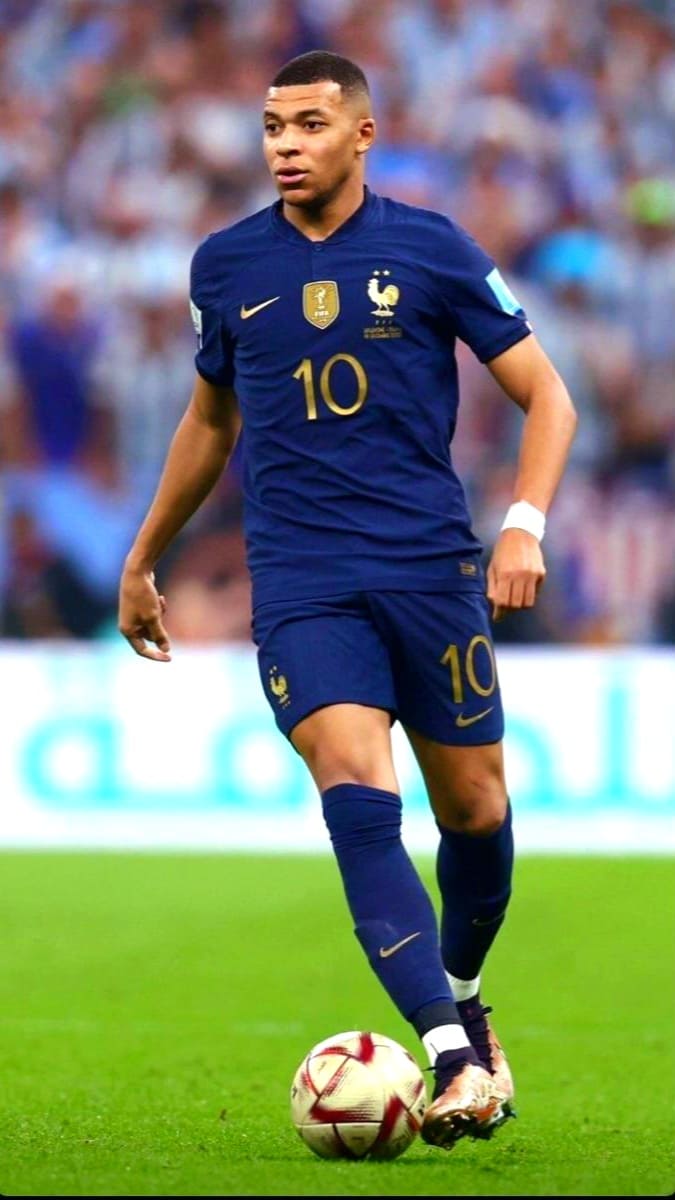 A football player in a navy blue France jersey with the number 10 dribbles a ball on a grassy field during a match, his focus unwavering. Fans can catch every moment live, including this action, on IPTV Latino. The crowd is blurred in the background.