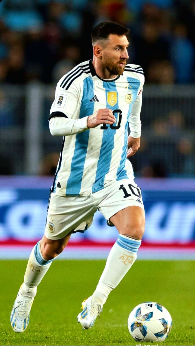 A male soccer player in an Argentina national team uniform dribbles a soccer ball on the field during a match, wearing a white and light blue striped jersey with the number 10. The action is perfect for streaming on IPTV Latino, with a blurred crowd in the background.